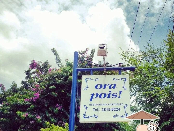 Placa do Ora Pois em poste azul entre árvores floridas