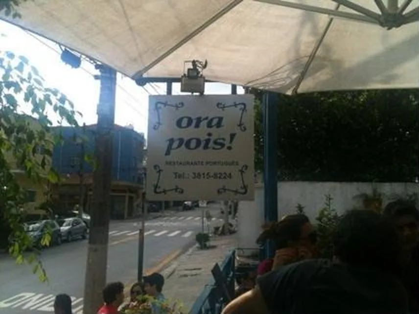 Área externa do Ora Pois com a placa azul e branca do restaurante